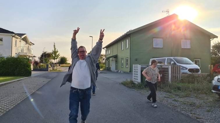 Leende man med funktionsnedsättning gör segergest utomhus på gata, kvinna går bakom.