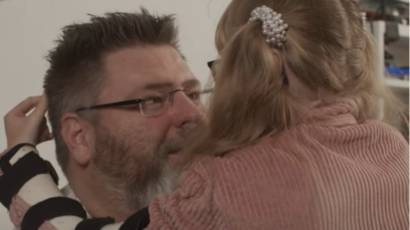 Man med glasögon ser kärleksfullt på hans dotter som kramar honom