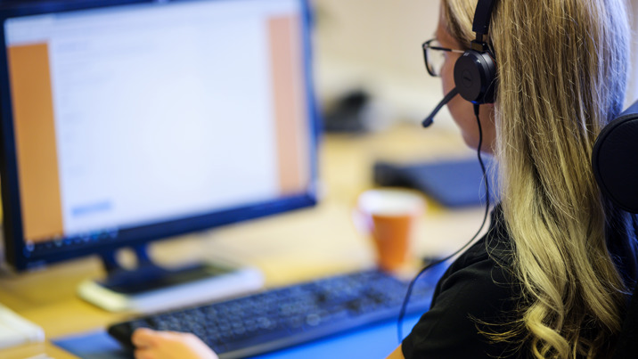Kvinnlig medarbetare med headset arbetar vid dator på kontor.