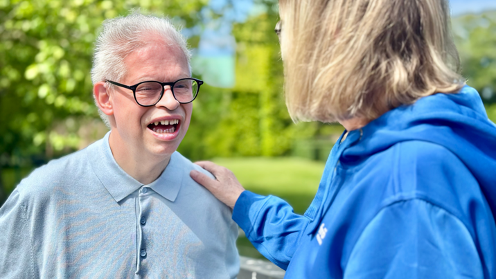 Leende man med glasögon pratar med kvinnlig assistent i blå hoodie utomhus