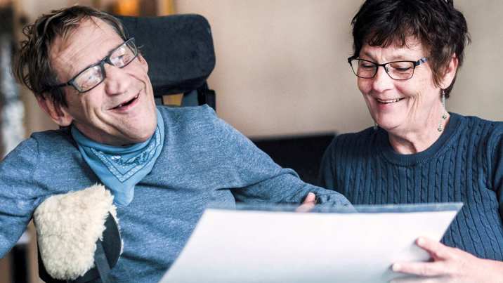 Man i rullstol och kvinnlig assistent tittar på kommunikationstavla tillsammans