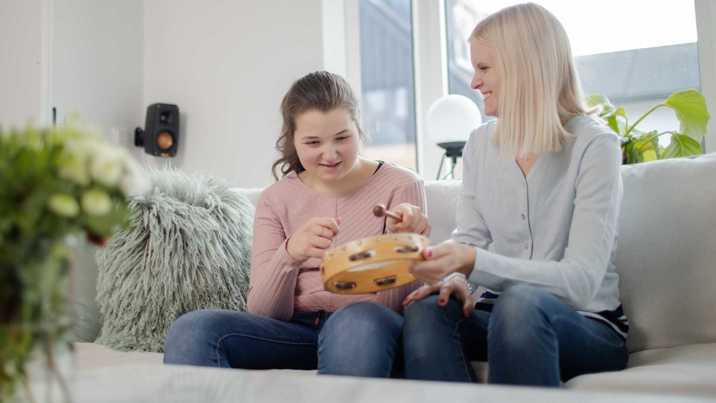 Ung tjej slår på tamburin medan assistent sitter bredvid och uppmuntrar