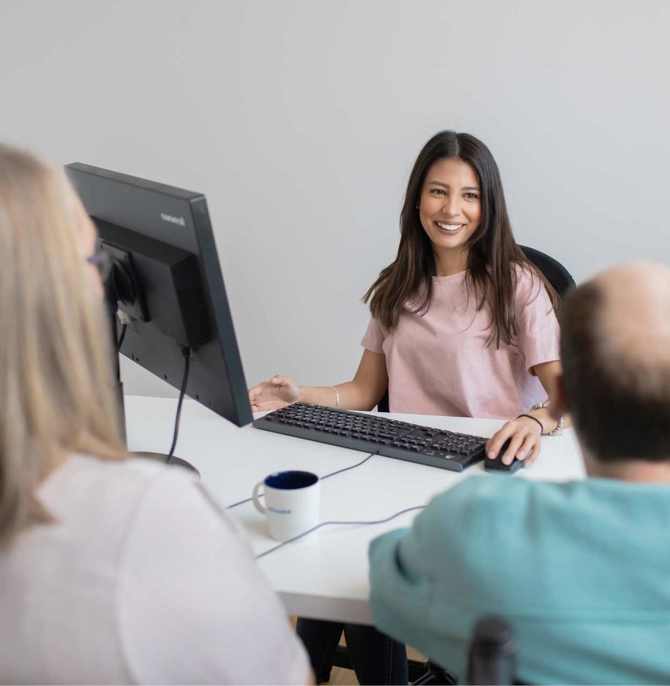 Leende kvinnlig medarbetare tar emot två besökare vid skrivbord på kontor.
