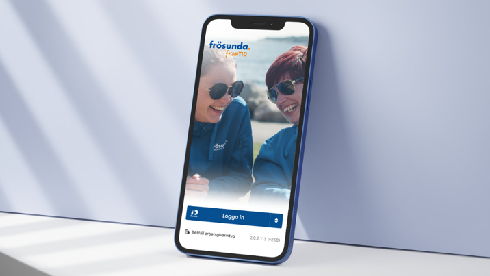 Mobil med Frösunda framTID-appen, visar kund med funktionsnedsättning tillsammans med personlig assistent på skärmen.